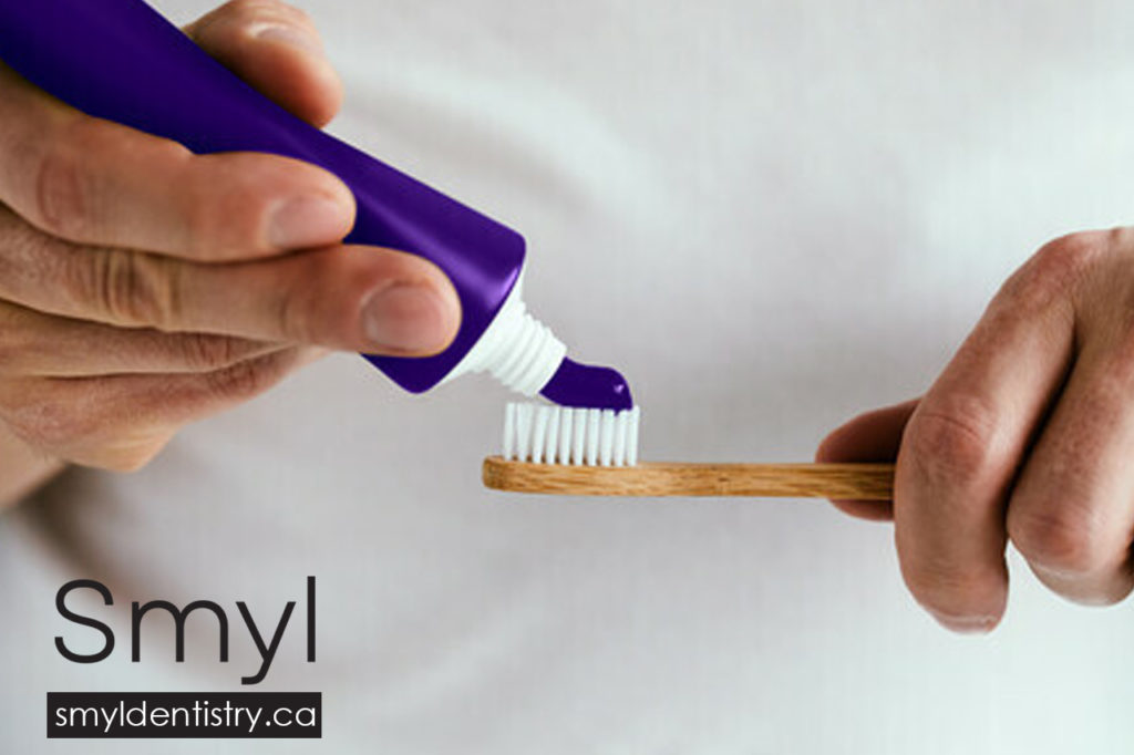 Purple toothpaste being applied to a brush.